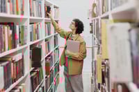 Person reaching for book on library shelf