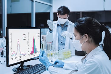 Scientists in lab with test tubes, looking at data on monitor