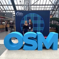 Two women standing behind large OSM sign