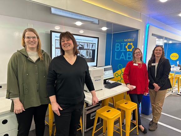 4 women standing at lab bench with FlowCam instrument