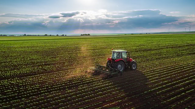Tractor in field of crops with sky and wind farm