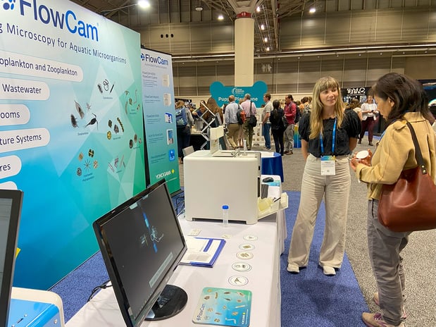FlowCam booth with monitor, graphics, woman presenting to visitor
