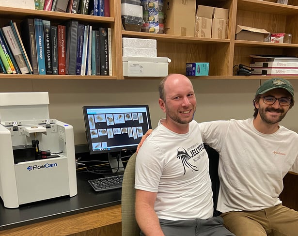 Two men sitting in front of a lab bench with a FlowCam instrument and monitor beind them.