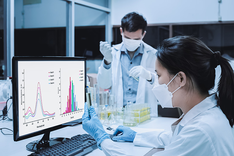 Scientists in lab holding test tubes looking at data on monitor